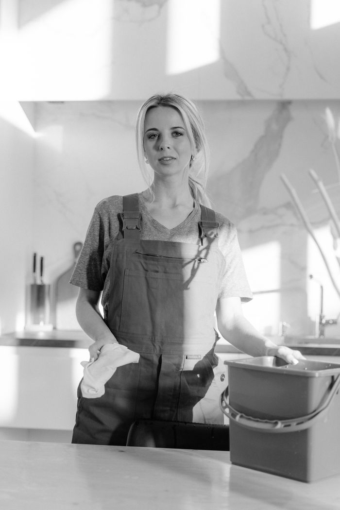 our-story Black and white portrait of a housekeeper with cleaning supplies in a modern kitchen.