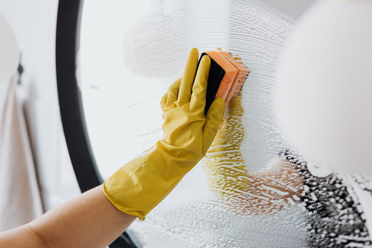 services-img Anonymous person in yellow rubber gloves using simple sponge for cleaning mirror in bathroom