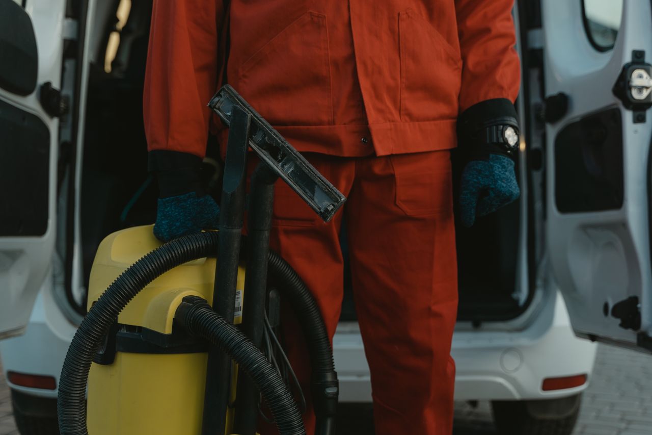 home-img A professional cleaner in a red uniform holding a vacuum near a van, ready for service.